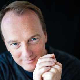 Marc Elsberg lächelt die Hände übereinander gelegt.