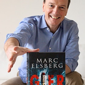 Marc Elsberg greift nach dem Buch „Gier“ und lächelt.