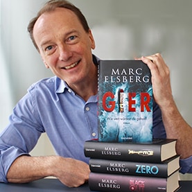 Marc Elsberg präsentiert das Buch „Gier“, welches auf einem Stapel seiner anderen Romane liegt.