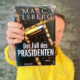 Marc Elsberg hält das Buch „Der Fall des Präsidenten“, in die Kamera.