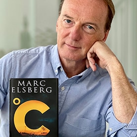 Marc Elsberg sitzt hinter seinem Roman Celsius auf einen Arm gestützt.